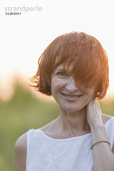 Portrait einer lächelnden Frau mit kurzen braunen Haaren  die im Freien stehen