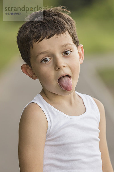 Portrait eines Jungen  der im Park die Zunge herausstreckt.