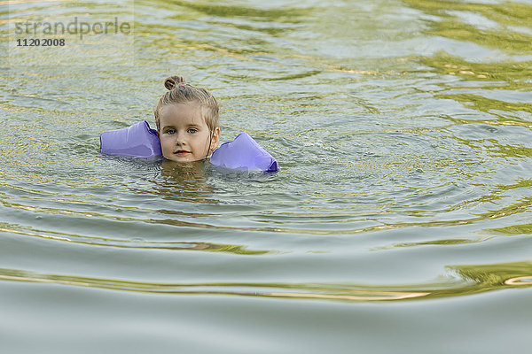 Porträt eines süßen Mädchens mit Schwimmflügeln im See