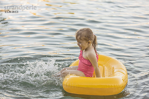 Fröhliches Mädchen sitzt auf dem Floß und spielt im See.