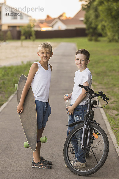 Lächelnde Freunde mit Skateboard und Fahrrad stehen im Park
