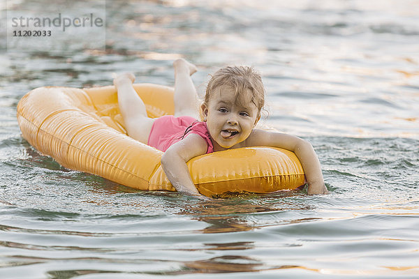 Heiteres süßes Mädchen  das auf einem Floß im See schwimmt.