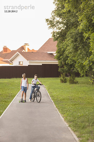 Freunde mit Skateboard und Fahrrad im Park gegen Häuser