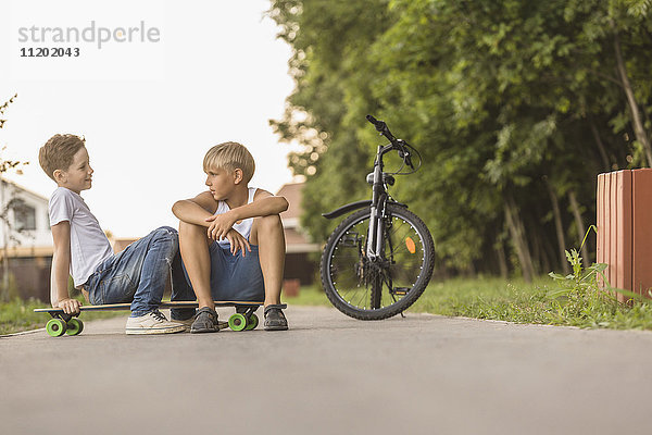 Freunde reden auf dem Skateboard mit dem Fahrrad im Park