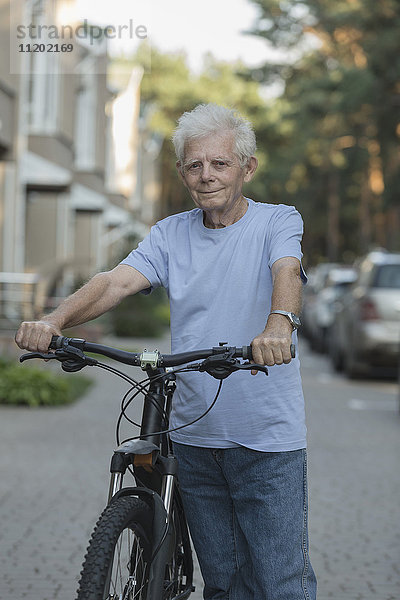 Portrait eines älteren Erwachsenen  der mit dem Fahrrad auf der Straße steht.