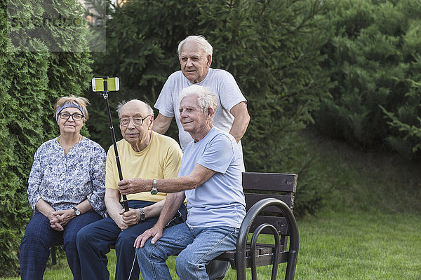 Lächelnde Seniorenfreunde  die sich mit einem Einbeinstativ auf der Parkbank selbstständig machen