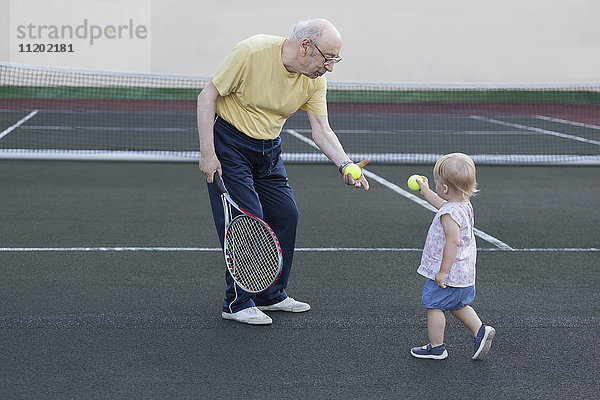 Mädchen gibt Großvater Tennisball  während sie auf dem Spielfeld steht.