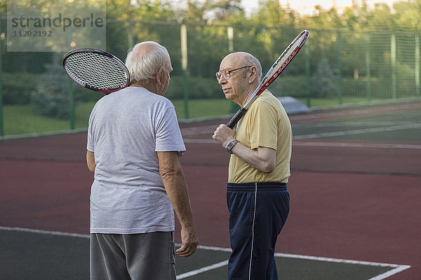 Seniorenfreunde  die Tennisschläger tragen  während sie sich auf dem Spielfeld unterhalten.