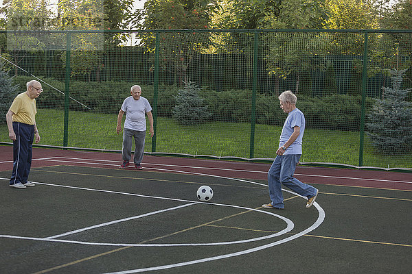 Seniorenfreunde spielen Fußball am Zaun auf dem Spielfeld