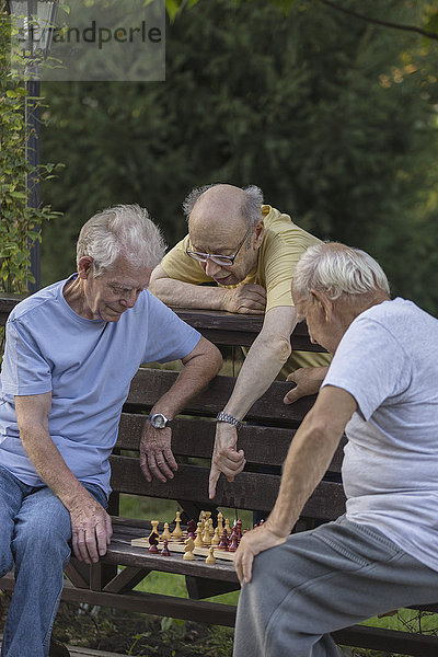 Älterer Mann  der Freunde beim Schachspielen im Park führt.