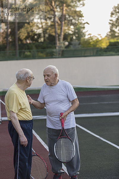 Ältere Freunde  die sich unterhalten  während sie Tennisschläger auf dem Platz halten.