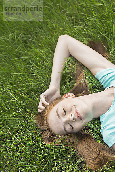 Hochwinkelansicht einer Frau  die mit geschlossenen Augen auf einem Grasfeld liegt.
