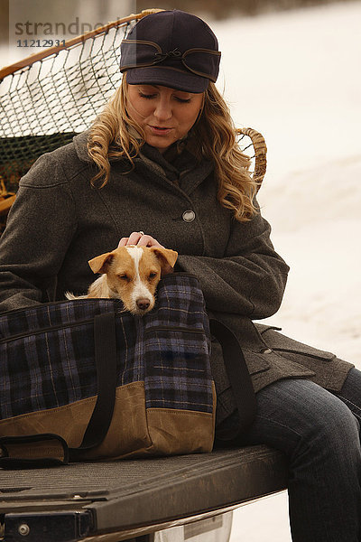 Frau in Winterkleidung hält einen Jack Russell Terrier auf der LKW-Heckklappe