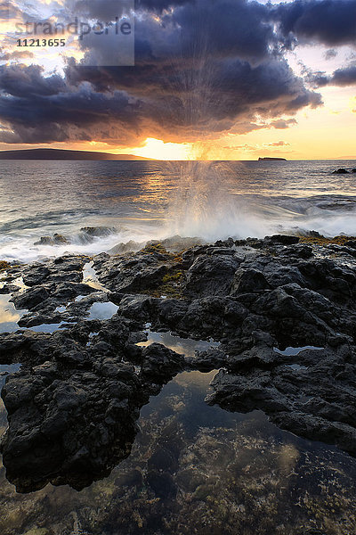 Wasser  das bei Sonnenuntergang auf das Lavagestein an der Küste spritzt; Hawaii  Vereinigte Staaten von Amerika'.