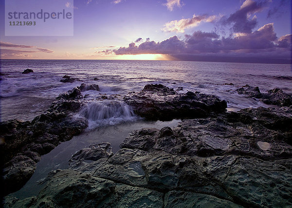Wasser plätschert auf dem schwarzen Lavagestein am Ufer  während die Sonne über dem Horizont untergeht; Hawaii  Vereinigte Staaten von Amerika'.