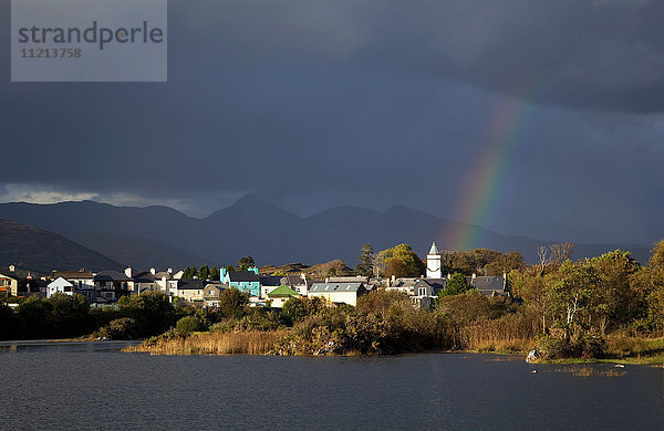 Ein Regenbogen  der durch die Gewitterwolken über einer Stadt scheint; Sneem  Grafschaft Kerry  Irland'.