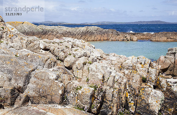 Zerklüftete Felsen entlang der Küste mit einer Lagune aus aquatischem Wasser und Bergen in der Ferne; Connemara  Grafschaft Galway  Irland