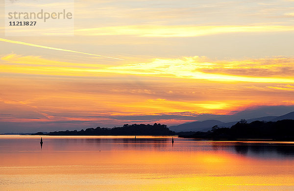 Ein dramatischer und farbenfroher Sonnenuntergang  der sich im Wasser spiegelt  mit Silhouetten der Küste und der Berge; Kenmore  County Kerry  Irland'.