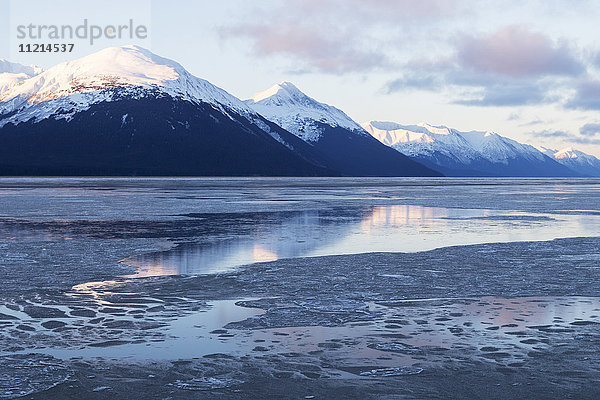 Eis auf dem Wasser des Turnagain Arm  mit schneebedeckten Bergen  die sich im Wasser spiegeln  südlich von Girdwood; Alaska  Vereinigte Staaten von Amerika'.