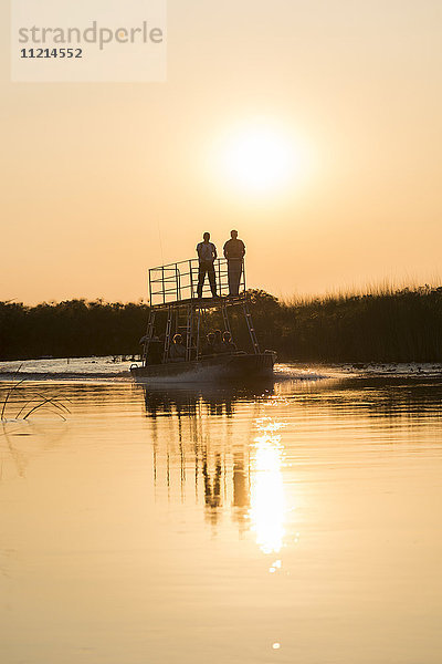Silhouette von Menschen auf einem Boot bei Sonnenuntergang; Botswana'.