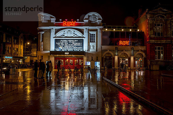 Lichter beleuchten Gebäude und spiegeln sich auf der nassen Straße  Brixton  South London; London  England'.