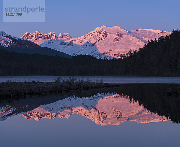 Rosa leuchtende Berge bei Sonnenaufgang und silhouettierter Wald  der sich in einem ruhigen See spiegelt; Juneau  Alaska  Vereinigte Staaten von Amerika'.