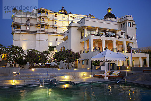 Blick in der Abenddämmerung auf das beleuchtete Devi Garh Heritage Palace Hotel und den Swimmingpool