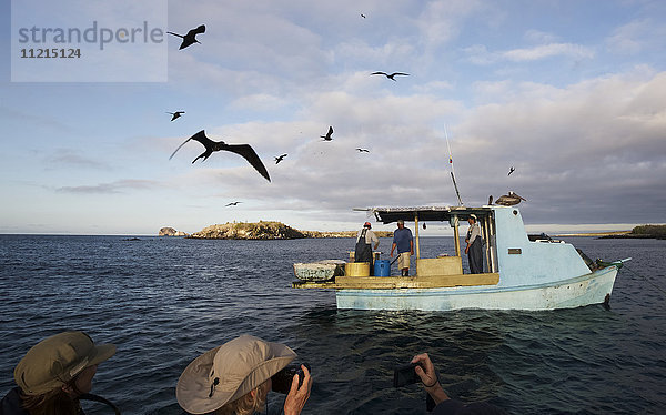 Fischer sortieren ihren Fang auf dem Boot  während Fregattvögel über sie hinwegfliegen