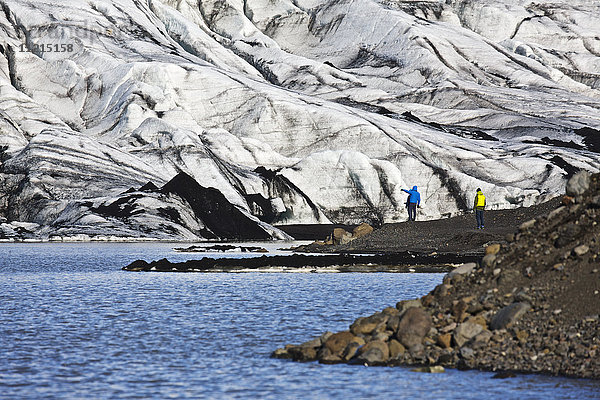 Wanderer am Ufer eines Sees neben einem schneebedeckten Gletscher  Südisland