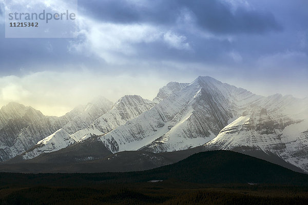 Schneebedeckte Bergkette mit silhouettierten Ausläufern  dunstige Wolken mit Schnee; Alberta  Kanada'.