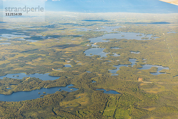 Luftaufnahme einer Straße  die durch tief liegendes Land mit Seen und Teichen führt  Süd-Zentral-Alaska; Alaska  Vereinigte Staaten von Amerika'.