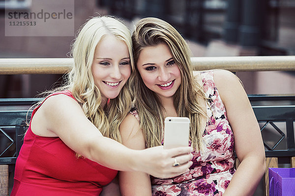Zwei schöne junge Frauen machen eine Pause  um ein Selfie zu machen  während sie zusammen in einem Einkaufszentrum einkaufen; Edmonton  Alberta  Kanada'.