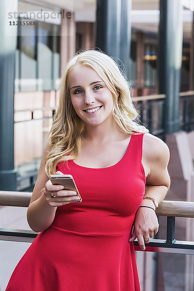 Eine hübsche junge Geschäftsfrau aus dem Millennium schreibt in einer Pause in einem Bürokomplex eine SMS und schaut in die Kamera; Edmonton  Alberta  Kanada .