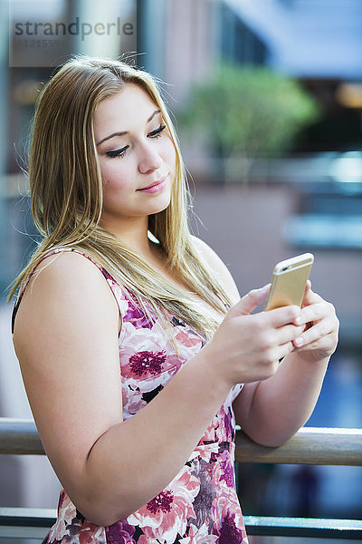 Eine hübsche junge Geschäftsfrau aus dem Millennium  die in der Lobby eines Bürogebäudes eine SMS auf ihrem Smartphone schreibt; Edmonton  Alberta  Kanada'.