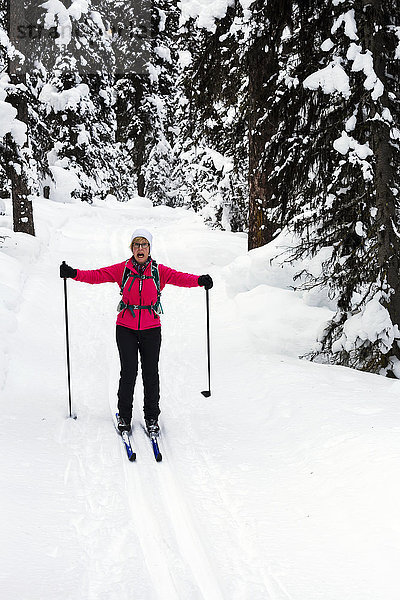 'Weibliche Langläuferin auf gespurter Loipe  die Arme seitlich ausgestreckt  bergab fahrend und mit aufgeregtem Gesichtsausdruck; Lake Louise  Alberta  Kanada'.