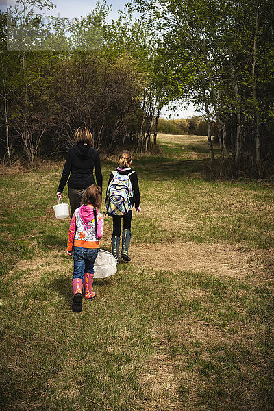 Eine Mutter geht mit zwei Töchtern einen Grasweg entlang  in der Hand einen Eimer und ein Netz; Saskatchewan  Kanada'.