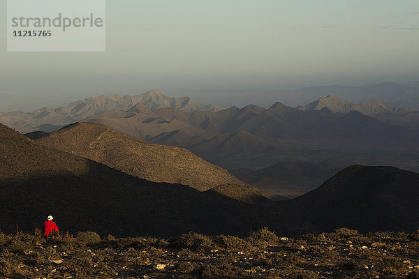 Frau sitzend mit Blick auf ein mit Bergen gefülltes Tal im Richterveld National Park; Südafrika'.