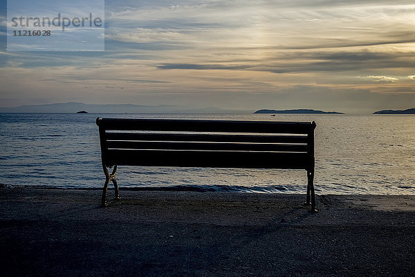 Silhouette einer Bank am Ufer eines Strandes bei Sonnenuntergang am Ägäischen Meer; Panormos  Thessalia Sterea Ellada  Griechenland'.