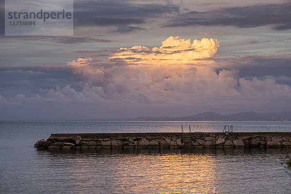 Ein steinerner Steg im ruhigen Wasser  in dem sich die glühenden Wolken bei Sonnenuntergang über dem Mittelmeer spiegeln; Lacco Ameno  Ischia  Neapel  Kampanien  Italien'.