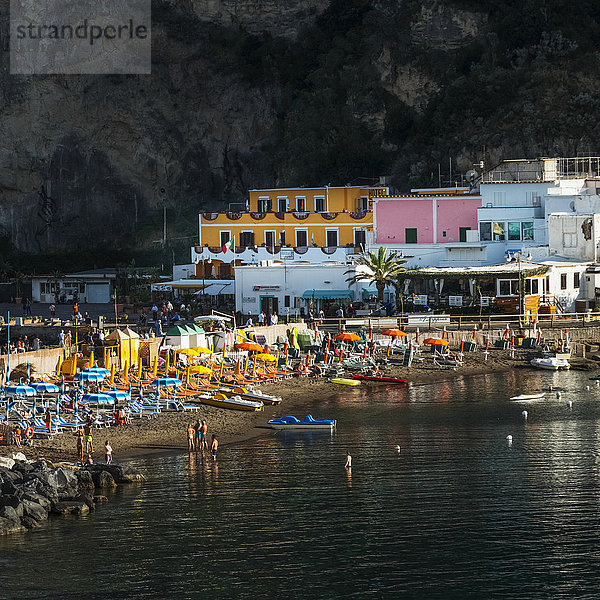Bunte Gebäude und Sonnenschirme  Stühle und Boote am Strand mit Schwimmern im Wasser; Sant Angelo  Ischia  Kampanien  Italien