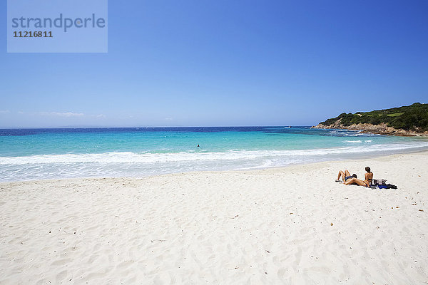 Paar beim Sonnenbaden am weißen Sandstrand mit türkisblauem Meer