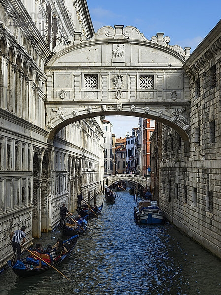 Dekorativer Torbogen über einem Kanal  der zwei Gebäude miteinander verbindet  mit Gondeln und Gondolieri  die den Kanal hinunterpaddeln; Venedig  Italien