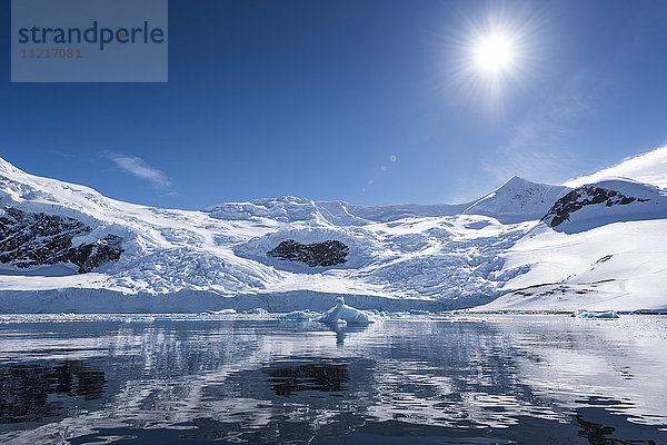 Strahlende Sonne und Schnee auf den Bergen  die sich im Wasser des Neko-Hafens spiegeln; Antarktis .