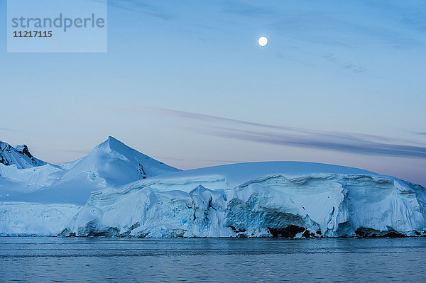 Vollmond am blauen Himmel über den schneebedeckten Bergen und dem blauen Meer; Antarktis'.