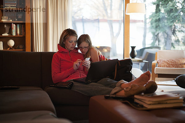 Mutter zu Hause mit Tochter  die ein Mobiltelefon und einen Laptop benutzt; Regina  Saskatchewan  Kanada