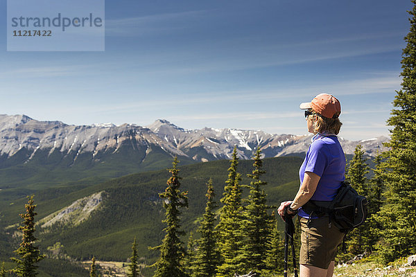 Wanderin mit Blick auf eine Bergkette in der Ferne  darunter ein Tal mit blauem Himmel und Wolken  Kananaskis Country; Alberta  Kanada'.