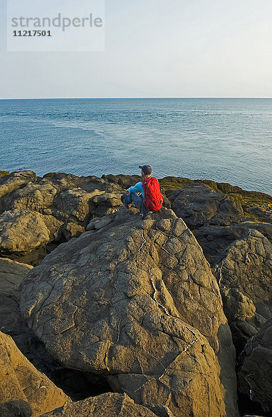 Wanderer sitzt auf einem Felsen mit Blick auf die Küstenlinie  Bay of Fundy; Long Island  Nova Scotia  Kanada'.