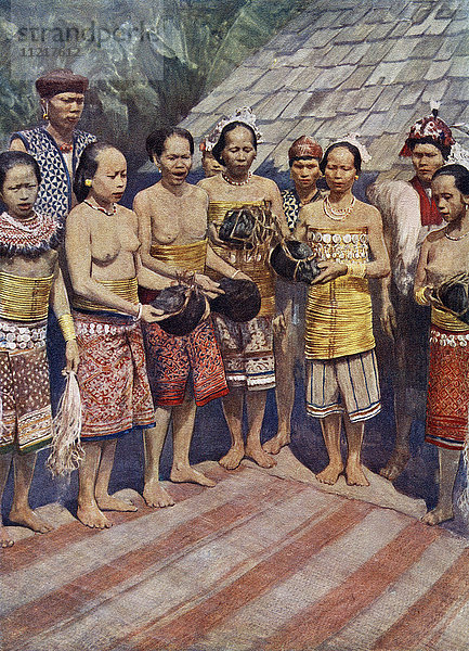 Dayak  Dyak- oder Dayuh-Frauen aus Borneo  Südostasien  tanzen mit menschlichen Köpfen. Einige Tage nach der Rückkehr von einer erfolgreichen Kopfjagd wurden die Köpfe  die von den toten Körpern abgehackt worden waren  ins Haus gebracht. Es folgte eine Zeit des Jubels  in der die Frauen die Köpfe an sich nahmen und sie nach fantastischen Tänzen neben die alten Köpfe hängten. Es wurde angenommen  dass die Anwesenheit der Köpfe im Haus die wohlwollenden Geister anlockt  die um sie herum leben. Aus Customs of The World  veröffentlicht ca. 1913.