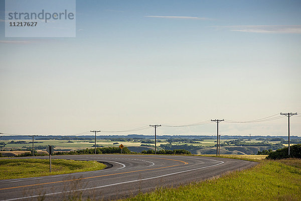 Elektrische Drähte entlang einer kurvenreichen Straße mit Farmland in der Ferne; Saskatchewan  Kanada'.