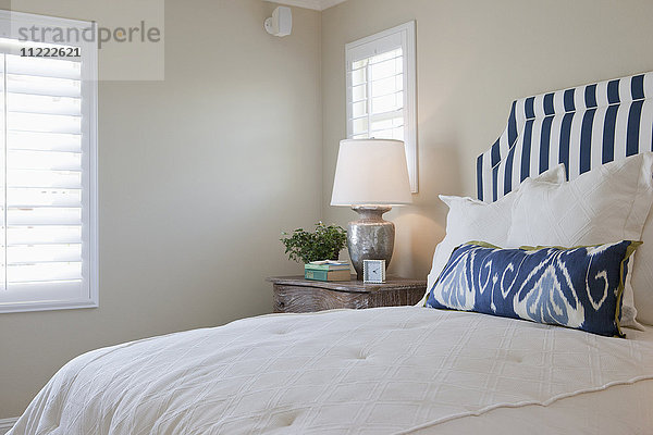 Arrangierte Kissen auf einem aufgeräumten Bett mit beleuchteter Tischlampe im Schlafzimmer zu Hause